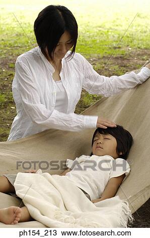 Stock Image - Young woman standing beside her daughter sleeping in a hammock. Fotosearch