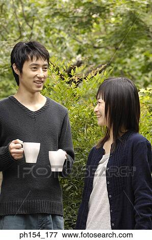 Stock Photo - Young woman standing with a young man holding coffee cups. Fotosearch