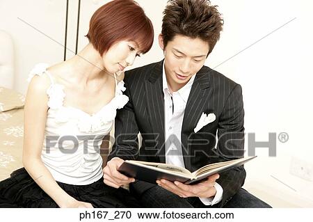 Stock Image - A couple sitting on edge of bed, reading. Fotosearch