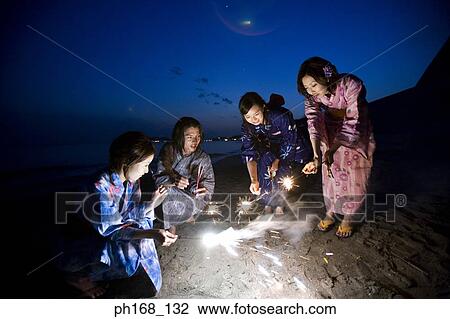 Stock Image - A small group of people with sparklers at the beach. Fotosearch
