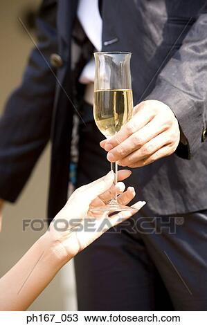 Stock Image - A young man handing a glass of champagne to a woman, close-up. Fotosearch