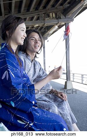 Stock Image - Couple in traditional Japanese clothing sitting at train station. Fotosearch