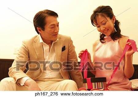 Stock Photograph - Man looking at woman unwrapping a present. Fotosearch