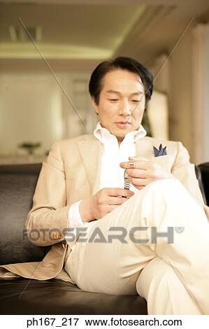 Man sitting at couch, holding a watch View Large Photo Image Stock Photo - Man sitting at couch, holding a watch. Fotosearch