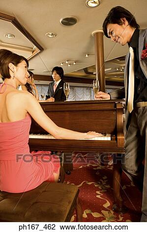 Man watching woman play the piano, with a couple standing by View Large Photo Image Stock Image - Man watching woman play the piano, with a couple standing by. Fotosearch