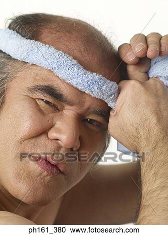 Stock Image - Mature man tying a blue towel around his head. Fotosearch