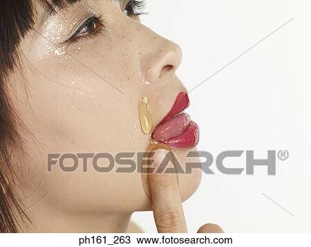 Stock Image - Portrait of woman licking her lips, with honey dripping down her face. Fotosearch