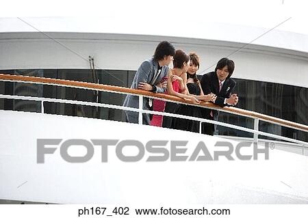 Stock Image - Two couple leaning on the railing onboard a cruise ship. Fotosearch