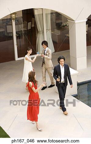 Stock Photograph - Two couples having cocktails and champagne in the courtyard, high angle. Fotosearch
