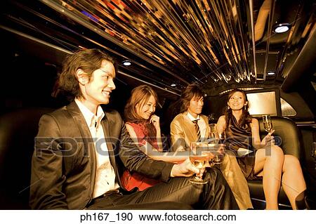 Stock Image - Two couples having wine and champagne inside a limousine. Fotosearch