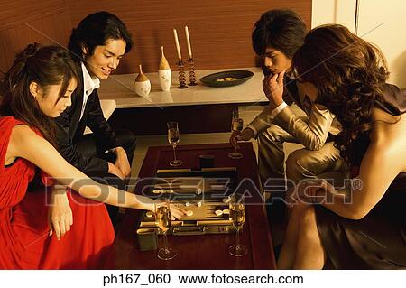 Stock Image - Two couples playing backgammon. Fotosearch