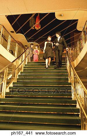 Stock Image - Two couples walking down steps of cruise ship, low angle view. Fotosearch