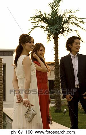 Stock Image - Two women and a man standing in courtyard, smiling. Fotosearch