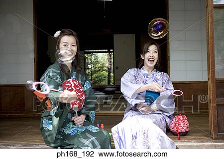 Stock Image - Two women in kimono playing with bubbles. Fotosearch