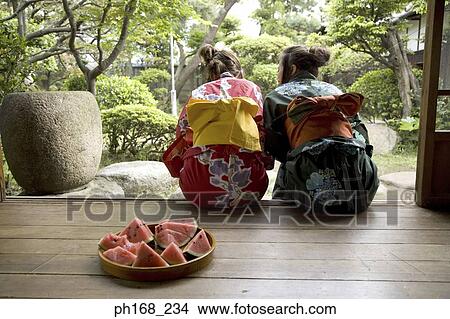 Two women sitting by corridor with a plate of water melon on the floor, rear view View Large Photo Image Picture - Two women sitting by corridor with a plate of water melon on the floor, rear view. Fotosearch