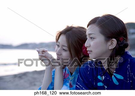 Stock Image - Two women sitting by the beach during sunset. Fotosearch