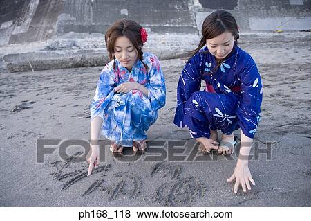 Two women writing on sand View Large Photo Image Stock Photo - Two women writing on sand. Fotosearch