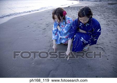 Two women writing on sand View Large Photo Image Stock Photo - Two women writing on sand. Fotosearch