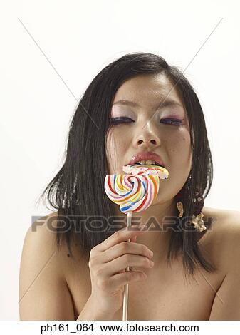 Picture - Woman biting a lollipop into half. Fotosearch