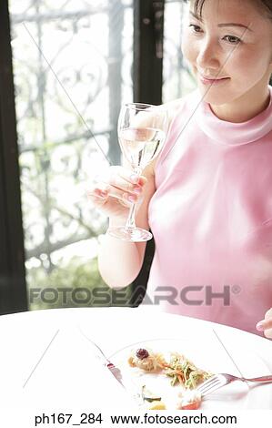 Picture - Woman eating in a restaurant with a glass of white wine. Fotosearch