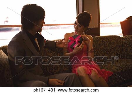 Woman holding a gift with man watching her View Large Photo Image Stock Image - Woman holding a gift with man watching her. Fotosearch