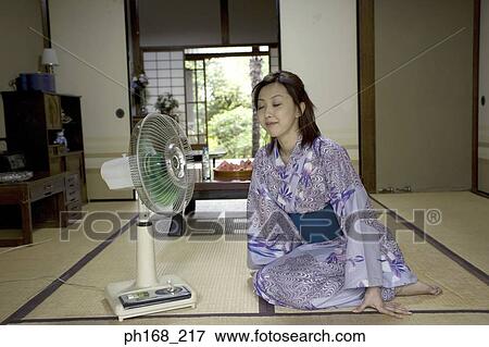 Stock Photo - Woman in kimono cooling herself in front of electric fan. Fotosearch