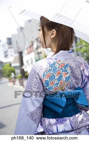 Stock Image - Woman in kimono, holding an umbrella, rear view. Fotosearch