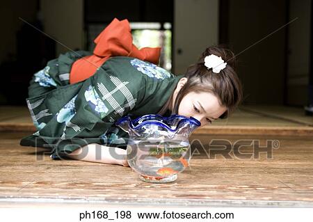 Stock Photo - Woman in kimono looking at fish tank. Fotosearch