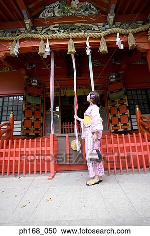 Stock Image - Woman in kimono tugging the rope at the temple. Fotosearch