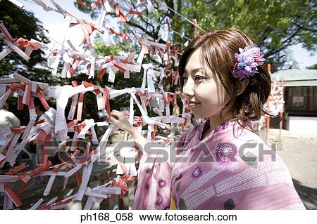 Stock Photo - Woman in kimono tying fortune slip on string. Fotosearch