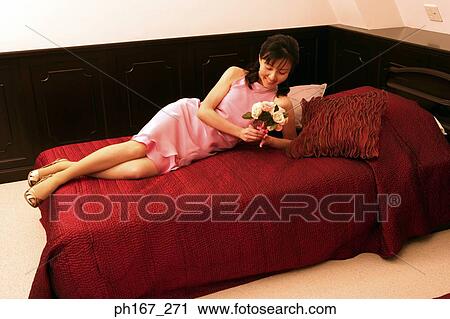 Stock Image - Woman lying on bed, holding a bouquet of flowers. Fotosearch