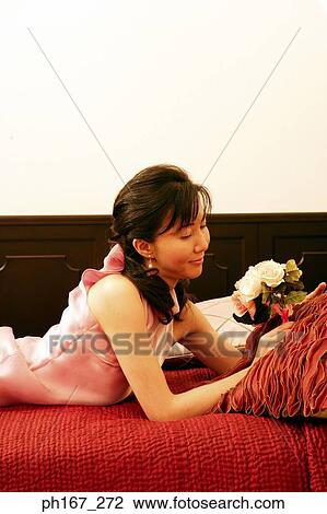 Stock Image - Woman lying on bed, holding a bouquet of flowers. Fotosearch