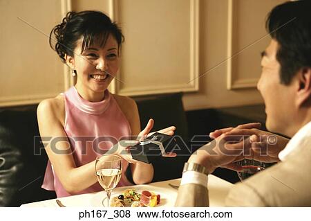 Stock Photo - Woman sitting by dining table, holding a gift. Fotosearch