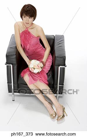 Stock Image - Woman sitting on a sofa with a bouquet of roses. Fotosearch