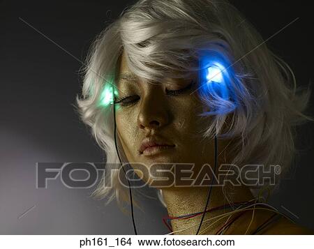 Woman wearing a blonde wig with gold paint on her face and body, and blinking headphones View Large Photo Image Picture - Woman wearing a blonde wig with gold paint on her face and body, and blinking headphones . Fotosearch