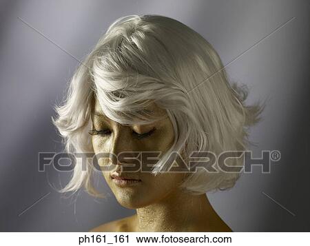 Stock Image - Woman wearing a blonde wig with gold paint on her face . Fotosearch