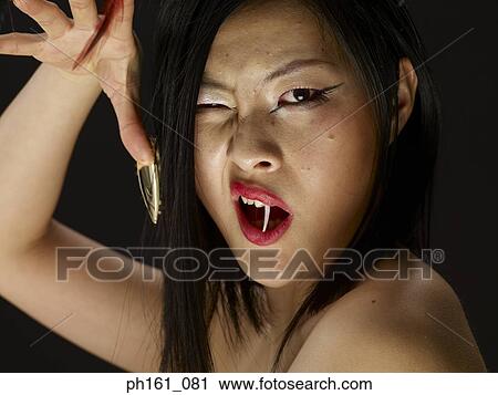 Stock Image - Woman with a fang and feathers on finger nails, posing. Fotosearch