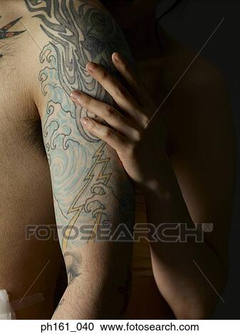 Stock Image - Woman's hand on the arms of man with tattoos. Fotosearch