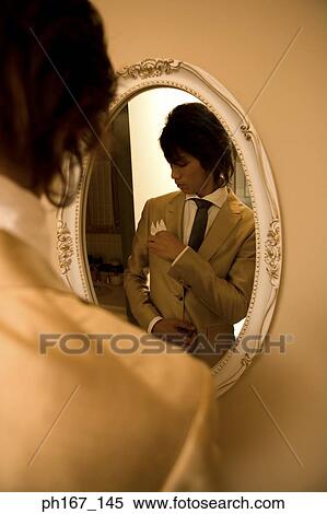 Stock Photography - Young man adjusting clothes in front of mirror. Fotosearch