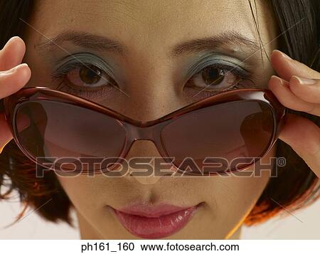 Young woman sliding sunglasses down nose, close-up View Large Photo Image Stock Image - Young woman sliding sunglasses down nose, close-up. Fotosearch