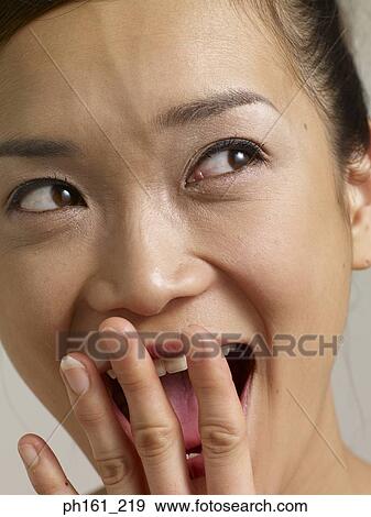 Stock Photo - Young woman with hand close to mouth, smiling. Fotosearch
