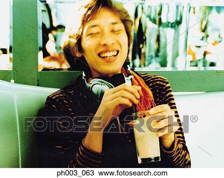 Stock Image - Asian man with Headphones laughing and holding beverage. Fotosearch