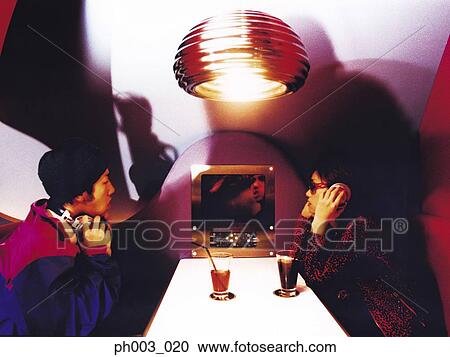 Stock Image - Young people listening to headphones in a restaurant. Fotosearch