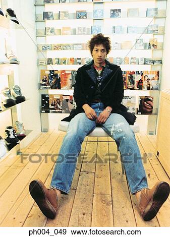Stock Photo - Man sitting in a cushion chair, book shelve in background. Fotosearch