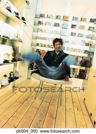 Man sitting in a cushion chair, legs raised, book shelve in background View Large Photo Image Stock Image - Man sitting in a cushion chair, legs raised, book shelve in background. Fotosearch