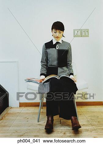 Stock Image - Woman reading in cushion chair. Fotosearch