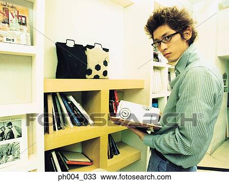 Stock Image - Young man reading book in novelty shop. Fotosearch
