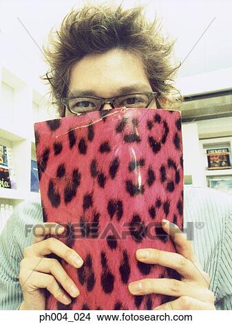 Picture - Young man uses magazine covering his face, showing eyes. Fotosearch