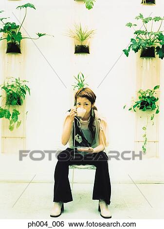 Young woman sitting and drinking beverage, potted plants decorated wall background View Large Photo Image Stock Photograph - Young woman sitting and drinking beverage, potted plants decorated wall background. Fotosearch
