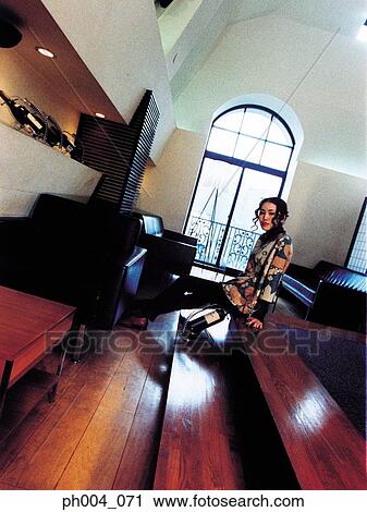 Stock Image - Young woman sitting on raised floor, bottle of wine. Fotosearch